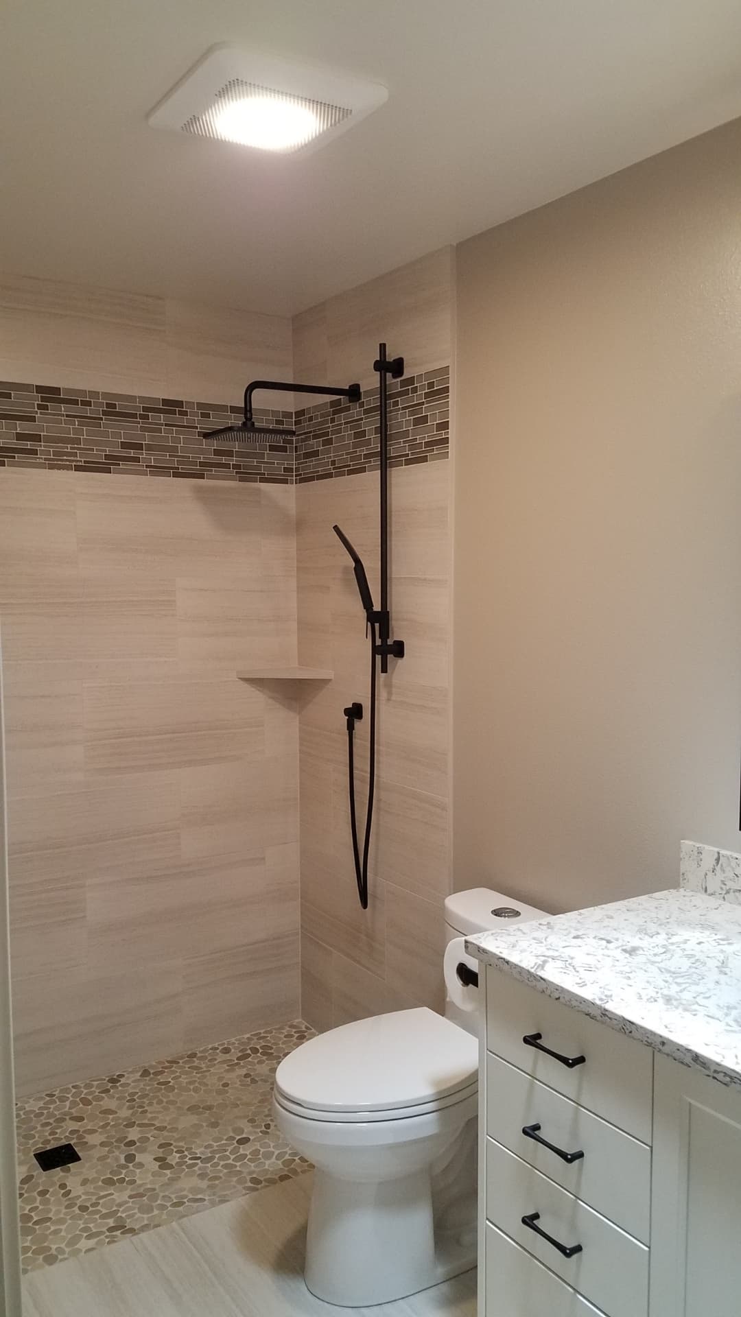 Beige walk-in shower with linear mosaic accent band, black fixtures and pebble floor