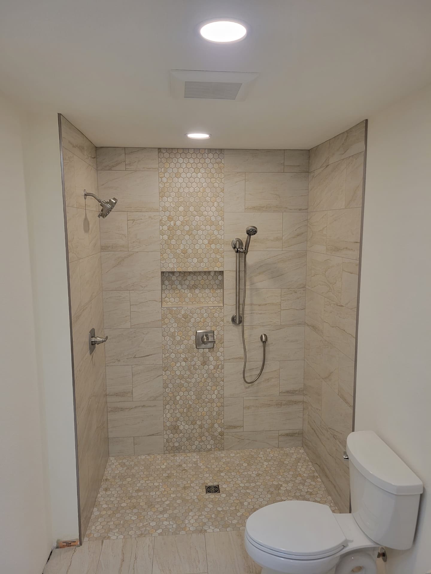 Curbless walk-in shower with hexagon mosaic accent column and recessed niche