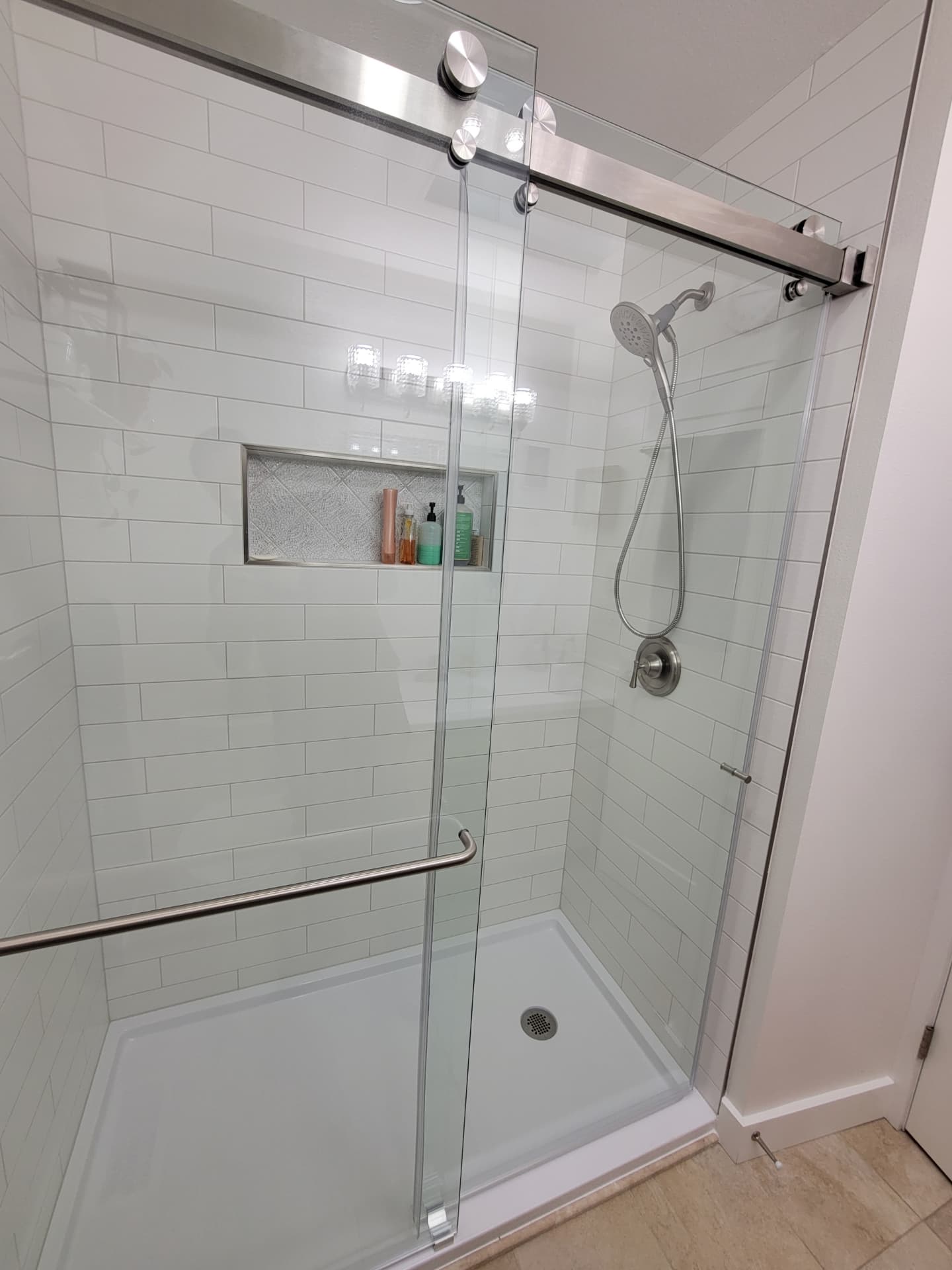 White subway tile shower with sliding glass enclosure and mosaic niche shelf