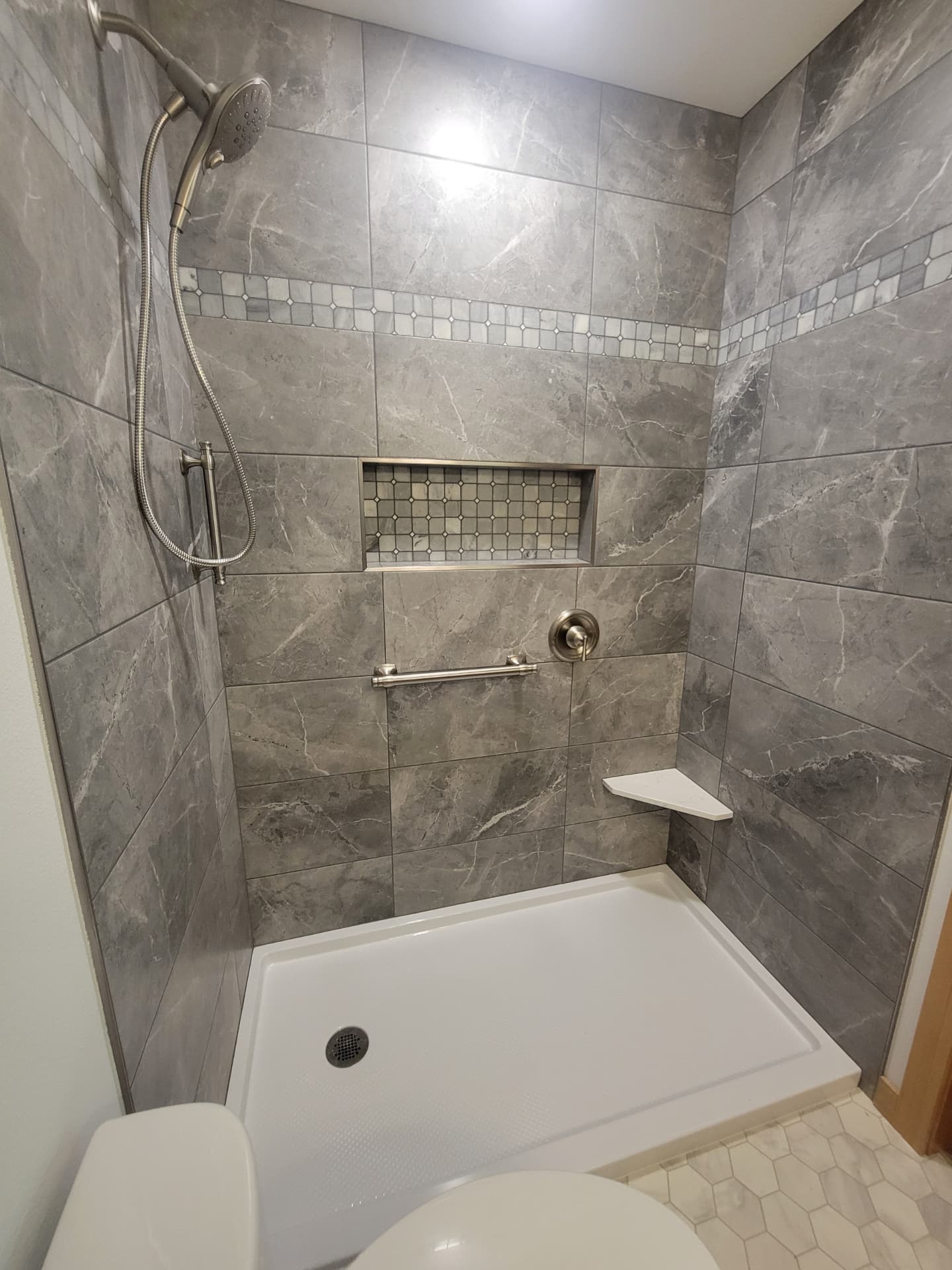Gray marble shower with decorative mosaic band, tiled niche and corner shelf