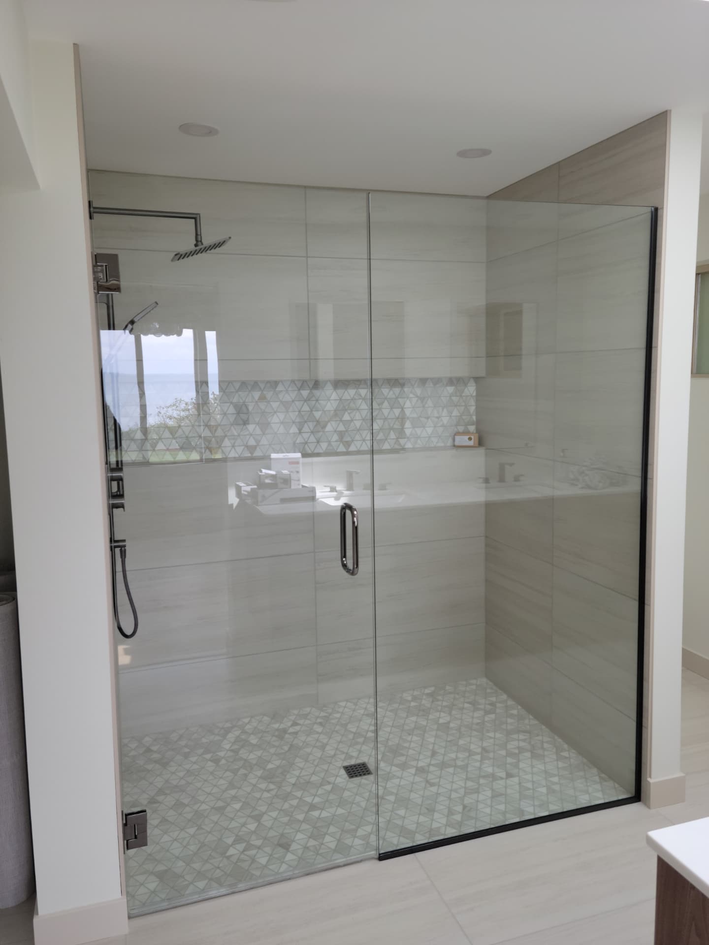 Large corner shower with floor-to-ceiling glass, light gray tile and triangle mosaic band