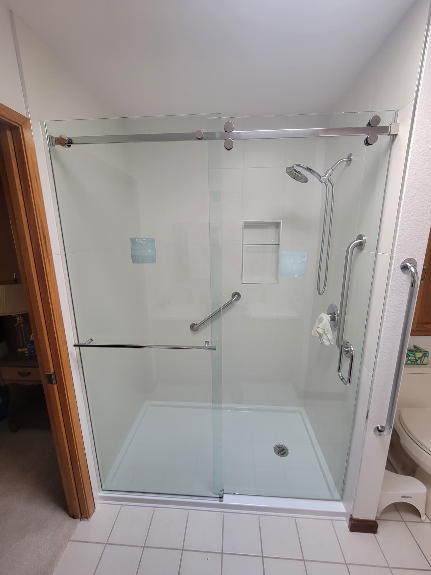 Accessible walk-in shower with sliding glass doors, grab bars and tiled niche