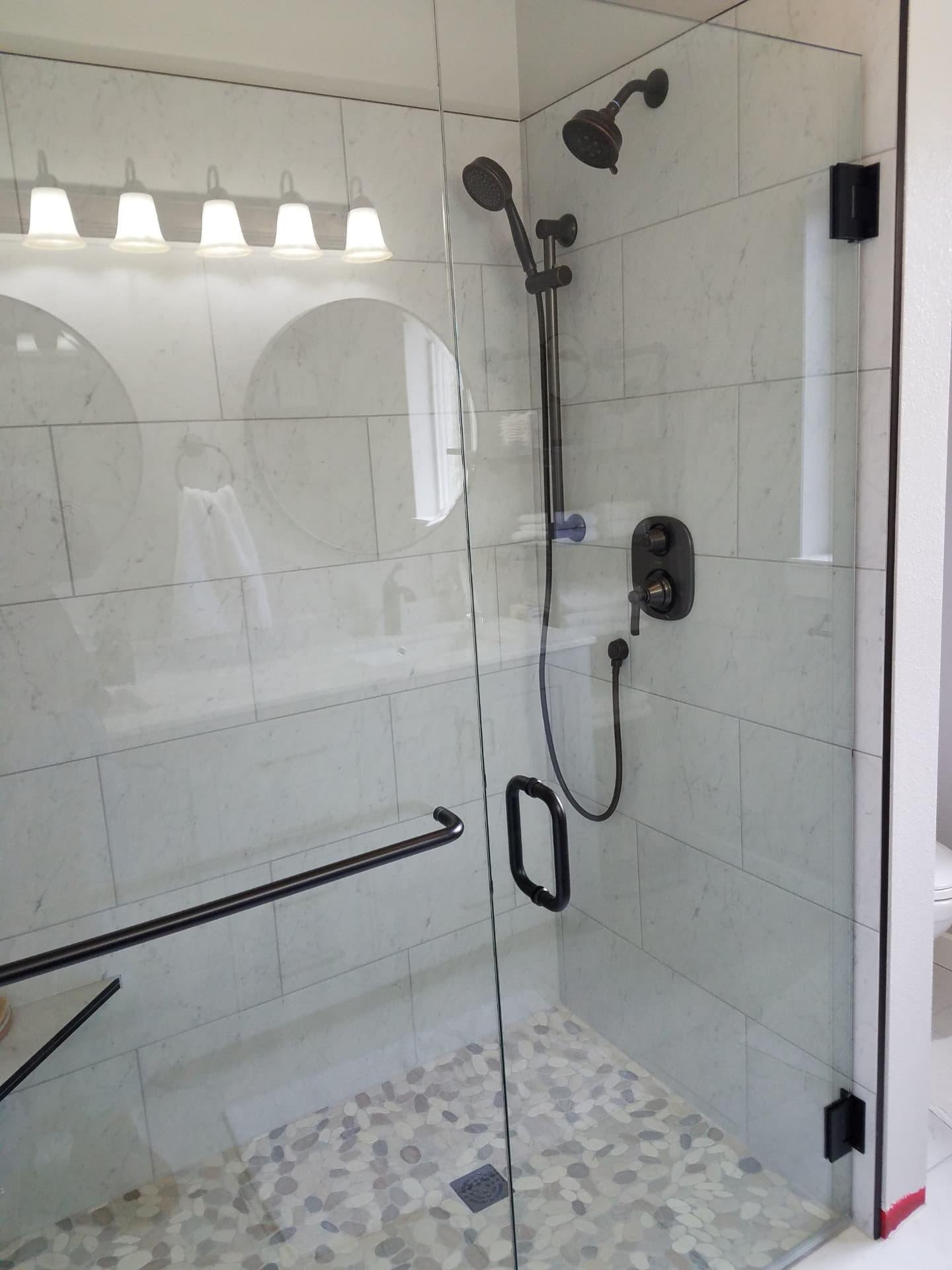 Frameless glass shower with marble-look tile, pebble floor and bronze fixtures