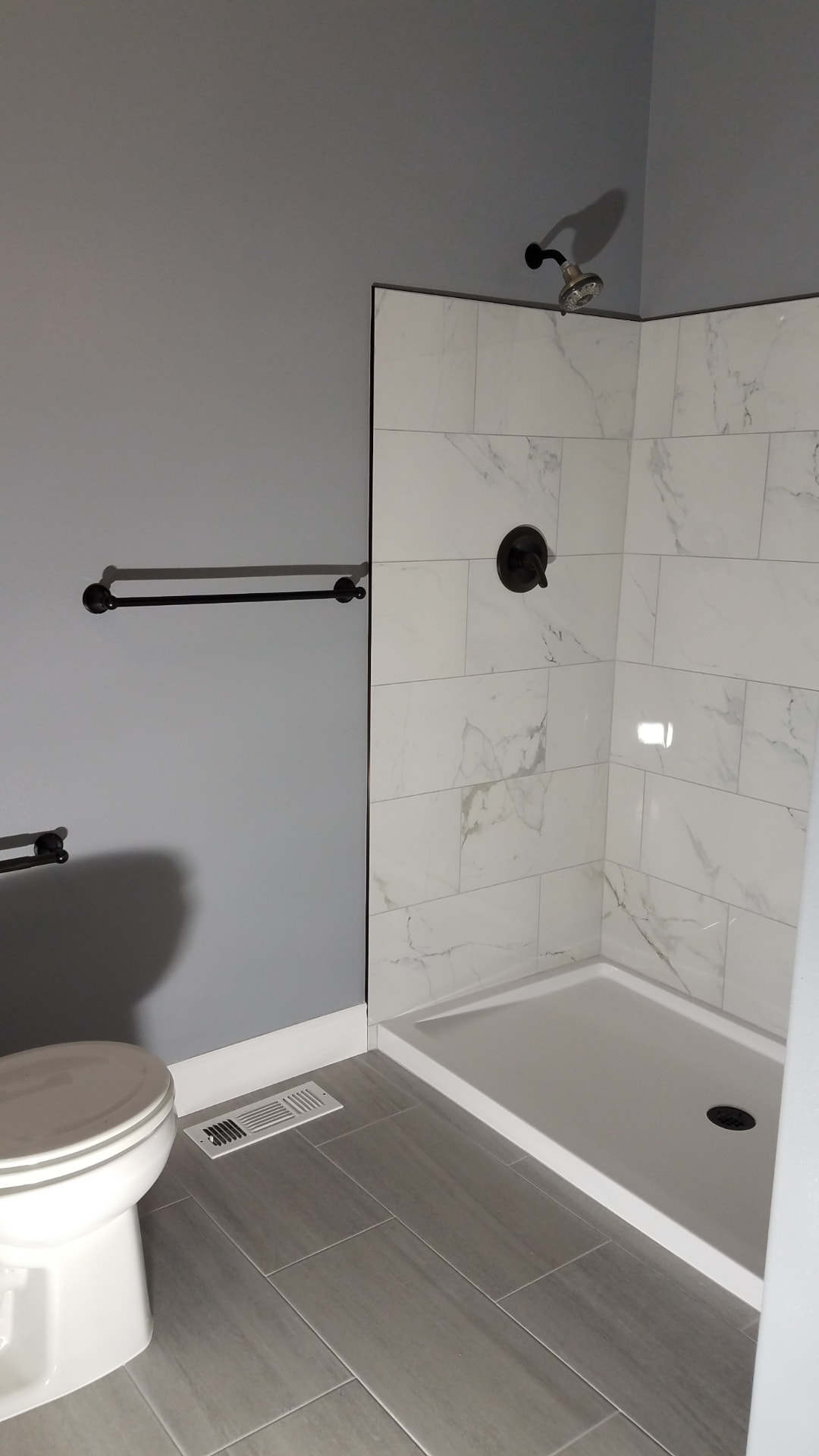 Marble-look tiled shower with gray walls, brushed nickel fixtures and white trim